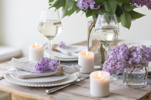 Beautiful table decor for a wedding dinner with a spring blooming lilac flowers. Celebration of a special event. Fancy white plates, wineglasses, candles. Countryside style